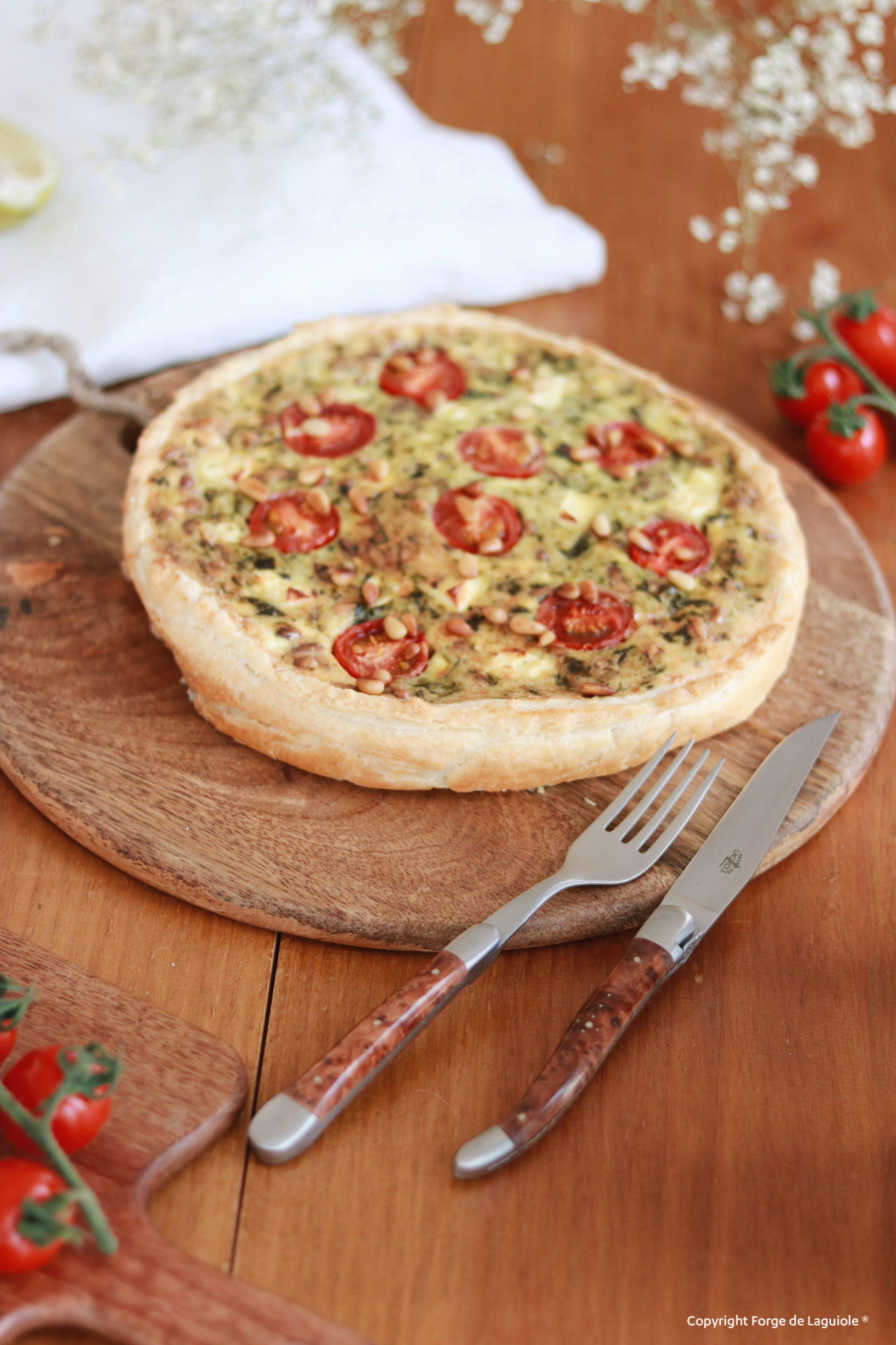 Herzhafte Quiche mit Tomaten und Pinienkernen, angerichtet auf einem runden Holzbrett mit Besteck
