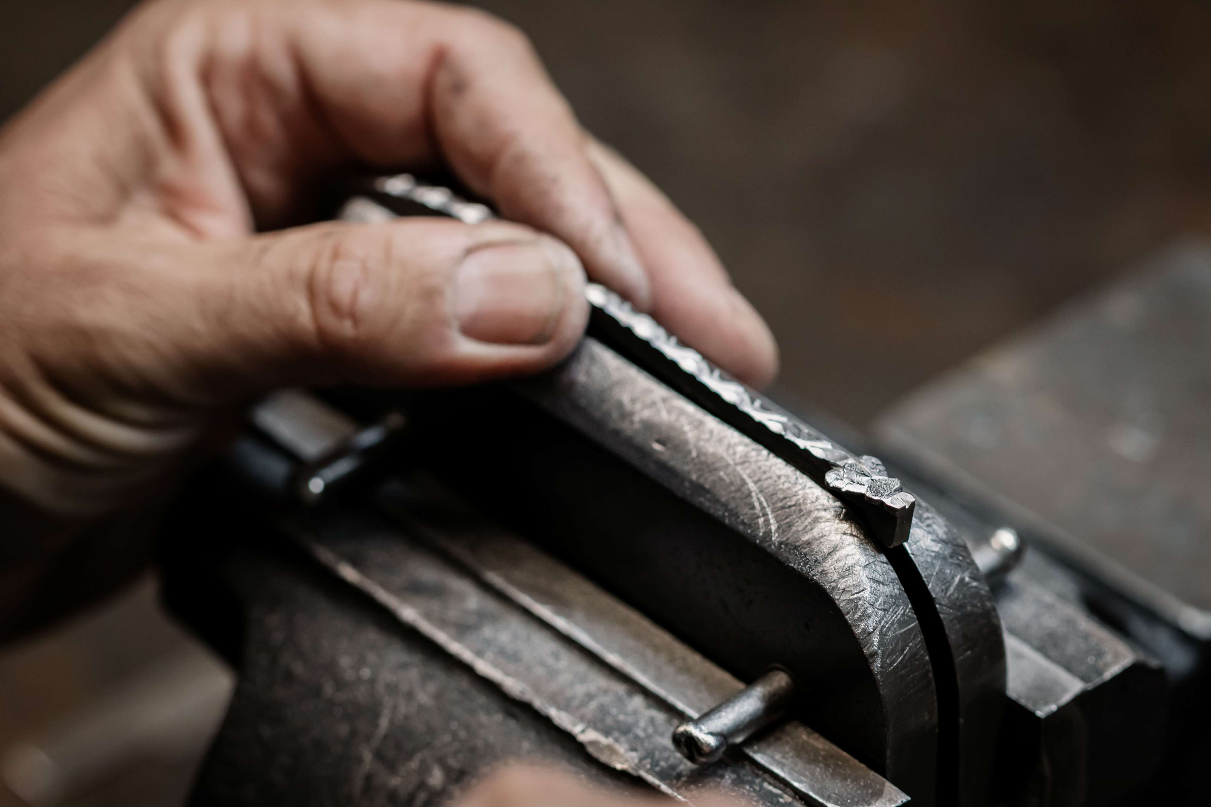 Nahaufnahme einer Hand, die ein geprägtes Metallstück in einem Schraubstock hält und bearbeitet.