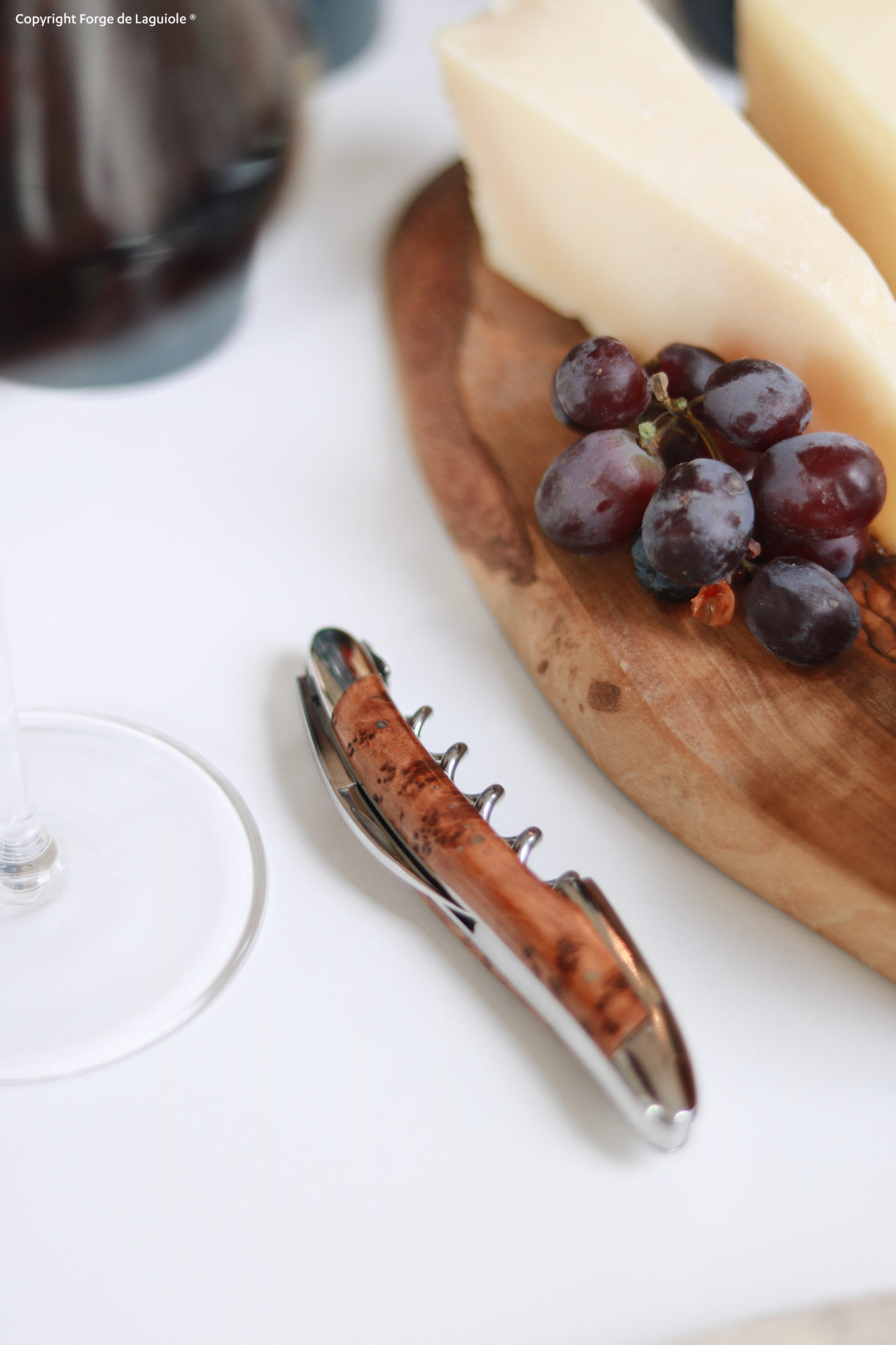 Korkenzieher mit Holzgriff liegt auf einem Tisch neben einem Glas Wein, Trauben und Käsestücken auf einem Holzbrett