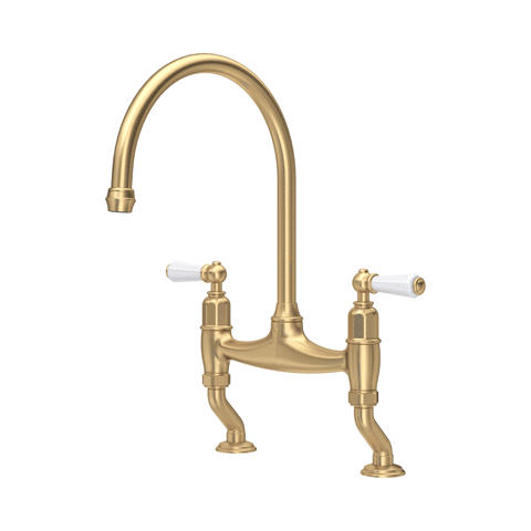 Klassische Küchenarmatur im Bridge-Design aus goldfarbenem Messing, Zweigriff mit weißen Keramikhebeln und hohem bogenförmigem Auslauf; ideal für die Spüle im Landhaus- oder Retro-Stil
