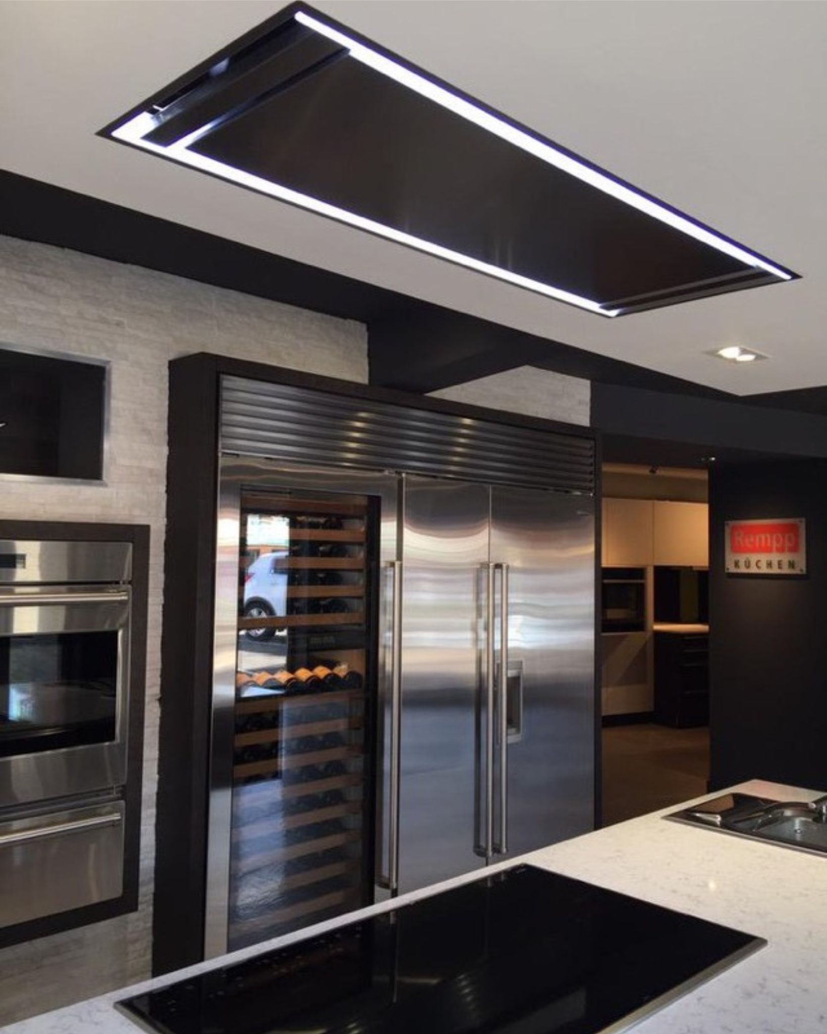 Designerküche mit Decken-Dunstabzugshaube, Weinkühlschrank, Edelstahl-Kühlschrank und Kochinsel mit Induktionskochfeld