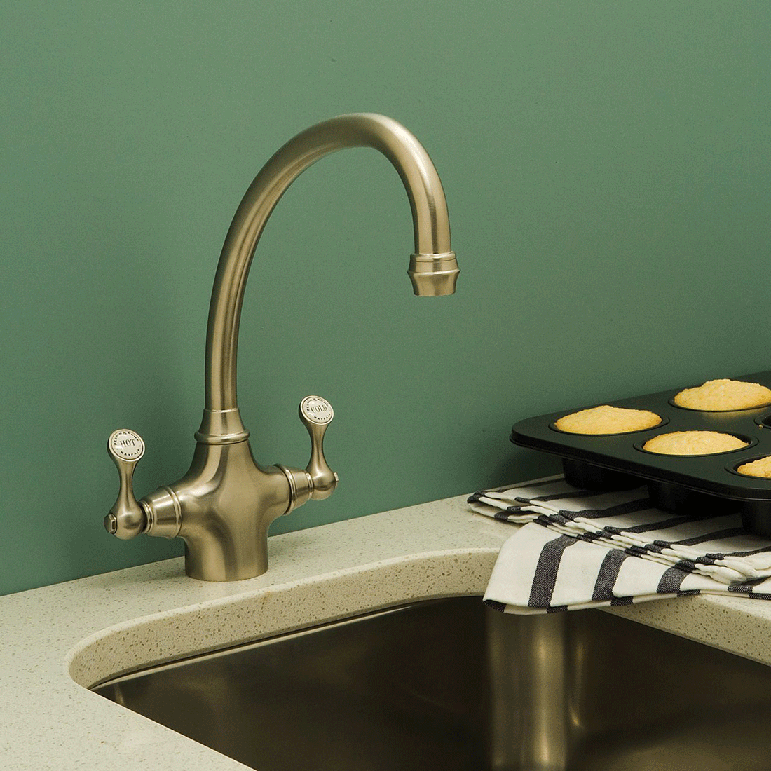 Moderne Küchenarmatur mit zwei Griffen für warmes und kaltes Wasser, daneben ein Muffinblech auf gestreiftem Geschirrtuch in einer stilvollen Küche