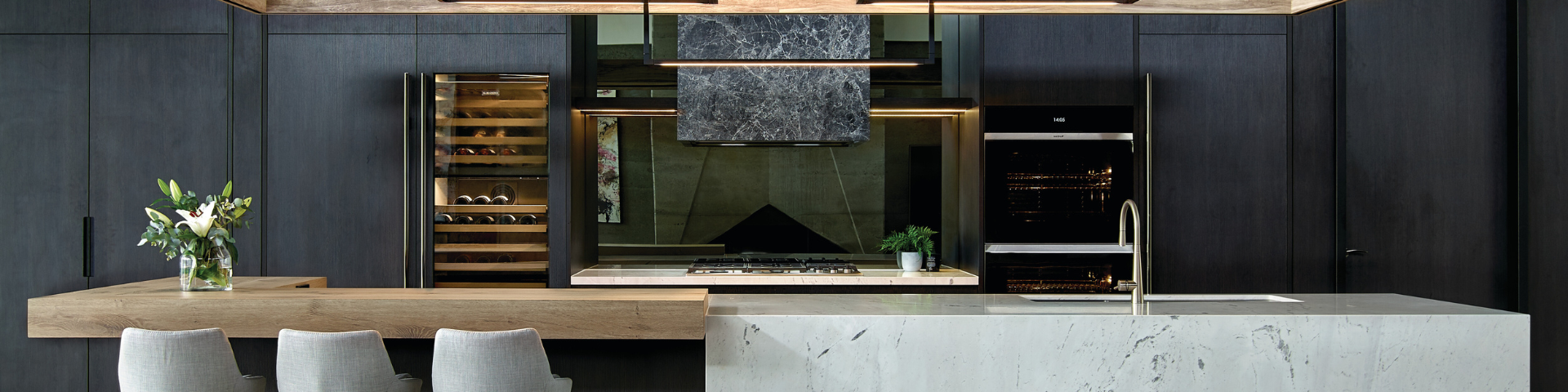 Elegante, moderne Küche mit dunklen Schränken, Marmorinsel, Weinkühlschrank, Backofen, Gaskochfeld und Blumendekoration auf einer Holztheke
