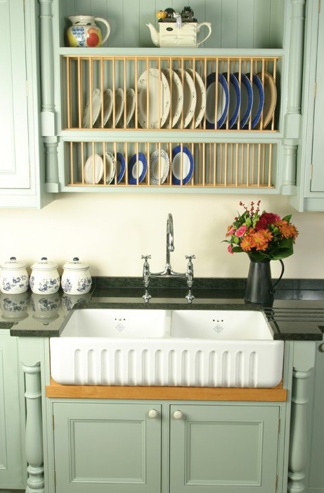 Küchenspüle im Landhausstil mit grünlichen Schränken, Tellerregal mit Geschirr und Blumenvase auf der Arbeitsplatte