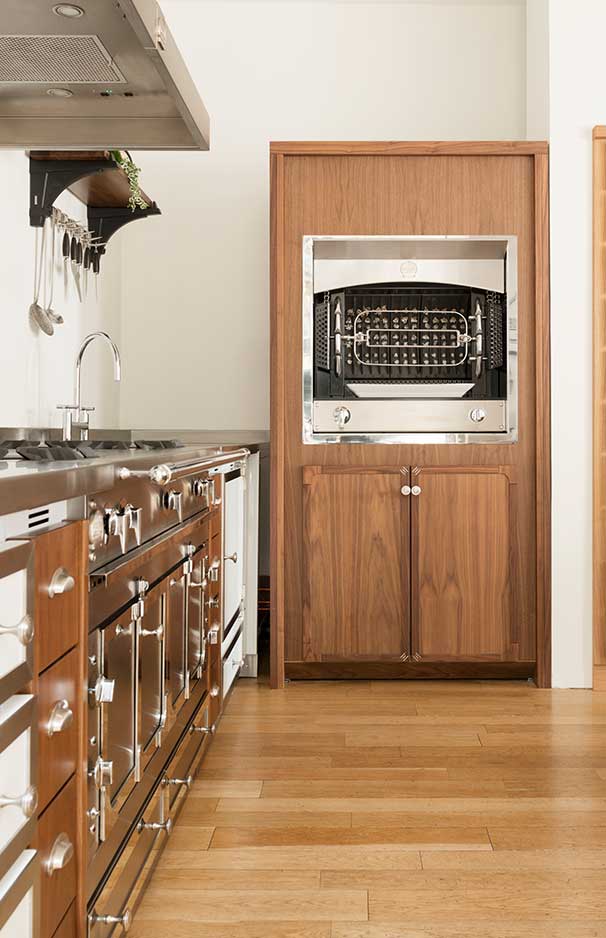 Geräumige, moderne Küche mit Edelstahl-Herd, Einbauspüle, Holzverkleidung und großem Grillofen, Küchenaccessoires an der Wand