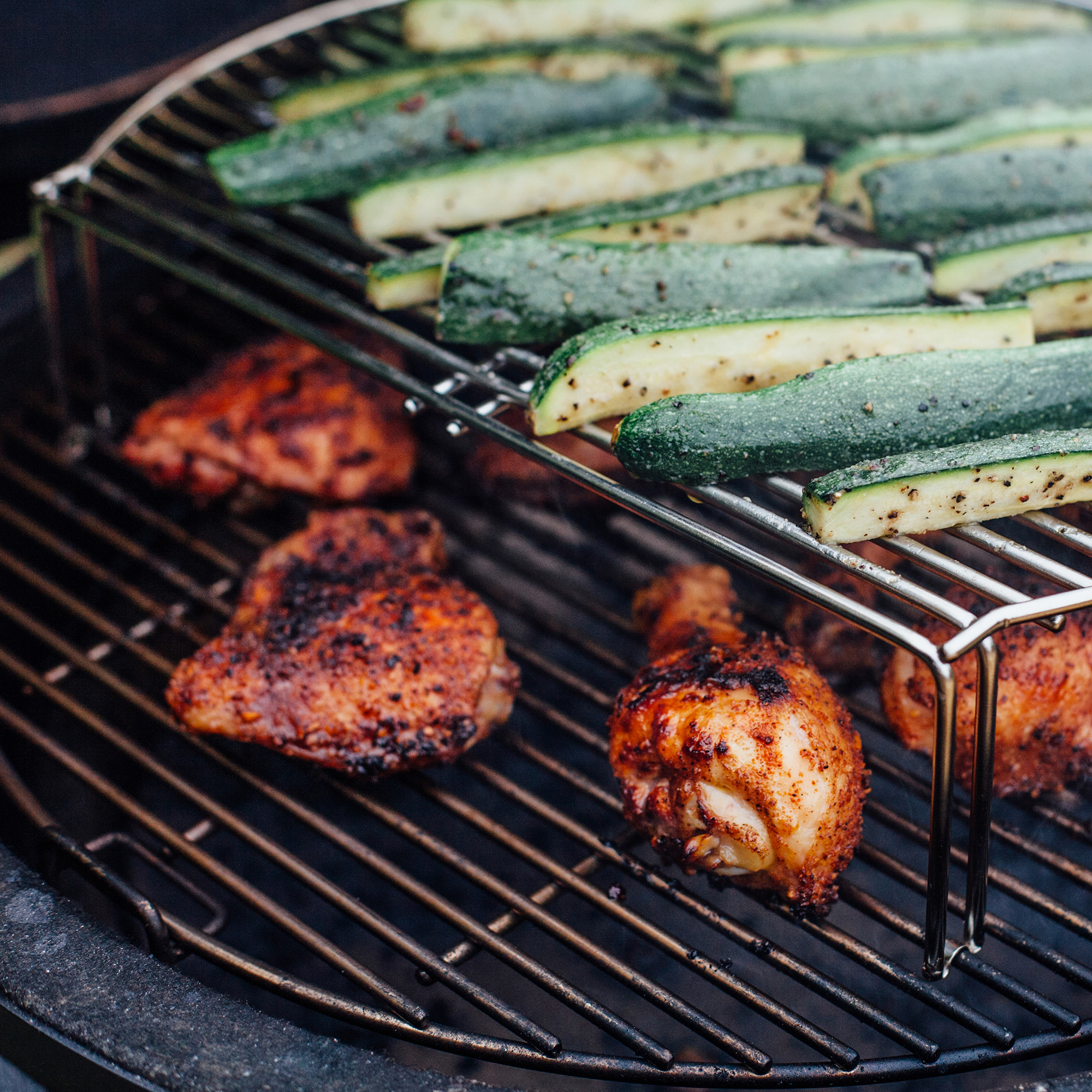 Frisch gewürzte Hähnchenschenkel und Zucchinistreifen auf einem Grill mit doppeltem Rost beim Grillen