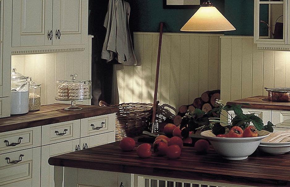 Stilvolle Landhausküche mit cremefarbenen Schränken, Holzarbeitsplatte, Obstschale mit Tomaten und einladender Atmosphäre
