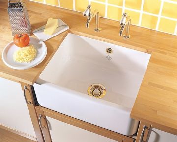 Weiße Keramikspüle eingebaut in eine Arbeitsplatte aus Holz, daneben geriebener Käse, Tomate und Käsereibe auf einem Teller vor gelbem Fliesenspiegel