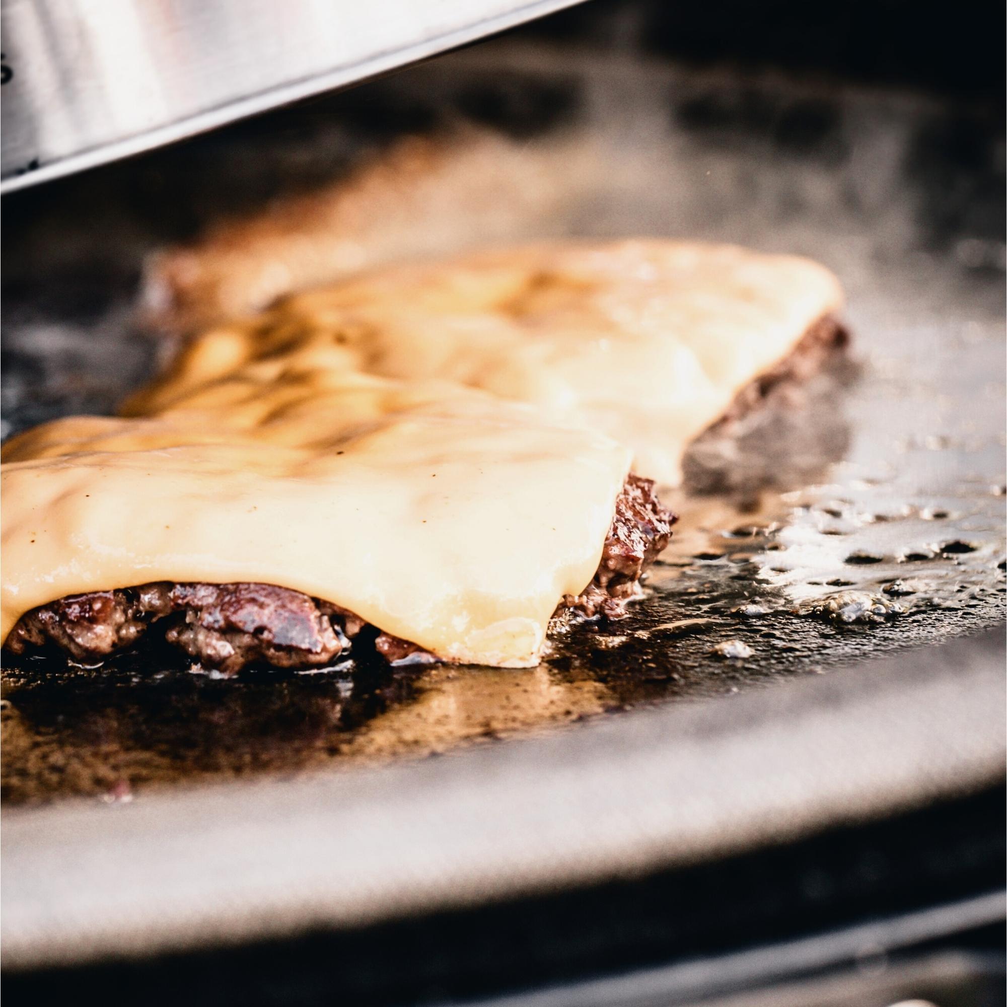 Zwei saftige Rindfleisch-Patties mit geschmolzenem Cheddar-Käse werden auf einer Grillplatte zubereitet