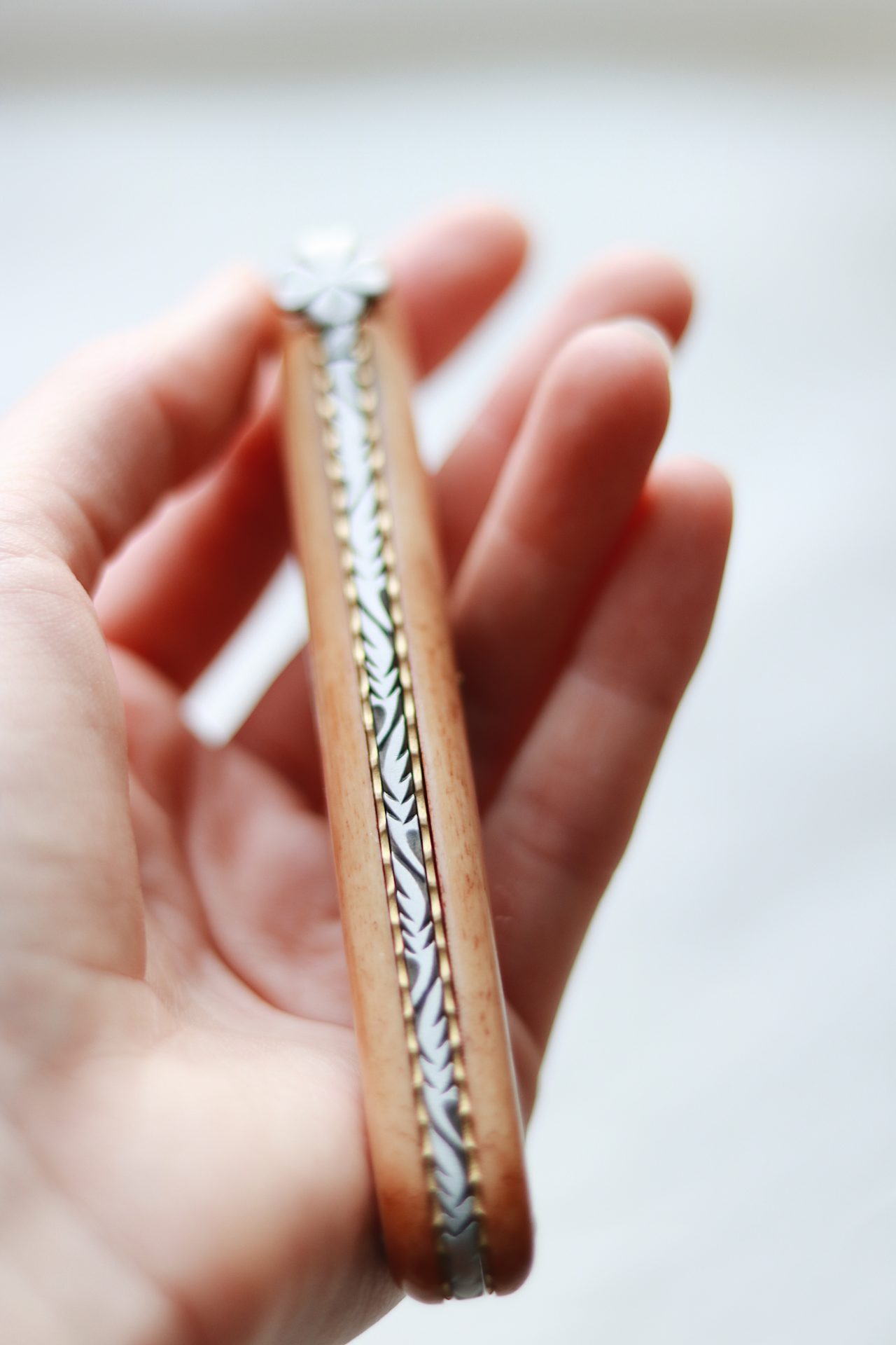 Hand hält ein edles, handgefertigtes Taschenmesser mit kunstvoll gestaltetem Metallmuster am Holzgriff