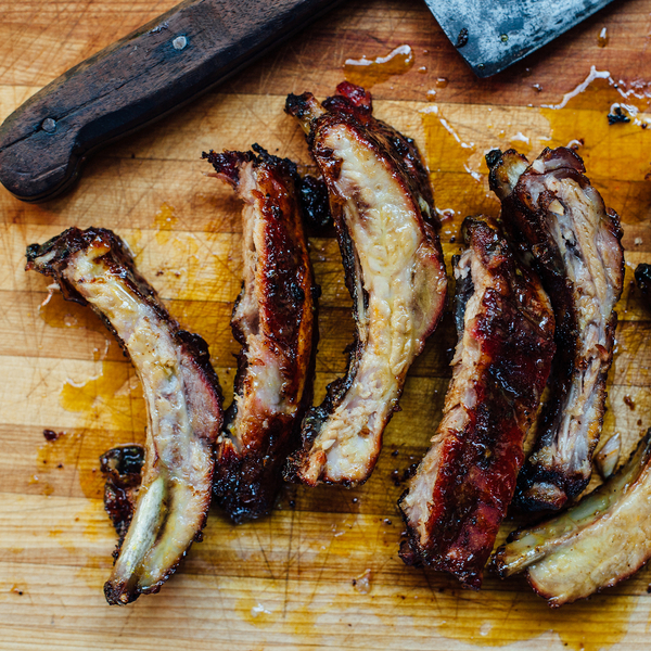 Mehrere knusprig gegrillte Spareribs liegen auf einem Holzbrett neben einem großen Küchenmesser