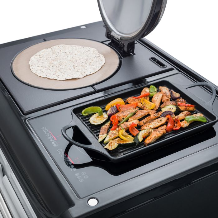 Modernes Induktionskochfeld mit Grillplatte, auf der bunt gemischtes Gemüse und Hähnchenfiletstreifen gegrillt werden, neben einem Fladenbrot auf einer runden Backfläche