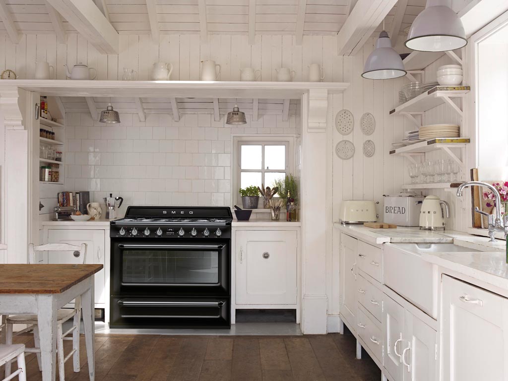 Gemütliche weiße Landhausküche mit schwarzem Smeg-Herd, Holzfußboden und vielen Küchendetails
