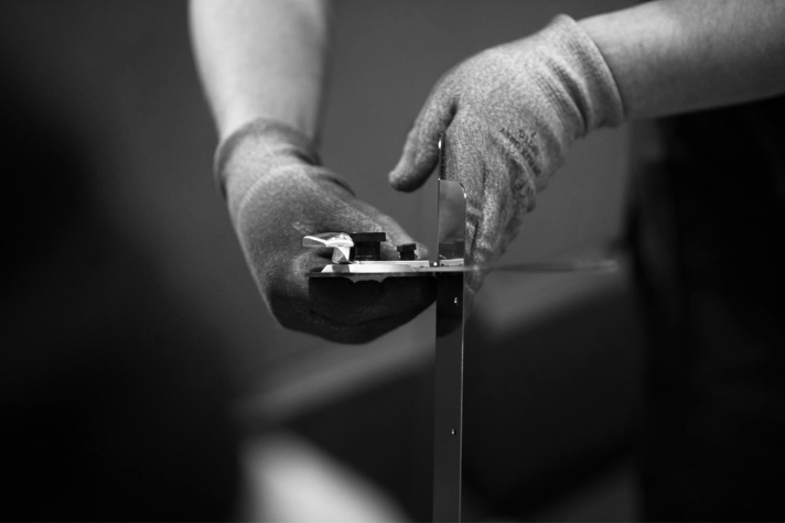 Nahaufnahme zweier Hände mit Arbeitshandschuhen, die Metallteile zusammenschrauben, Fokus auf Handwerk und Präzision