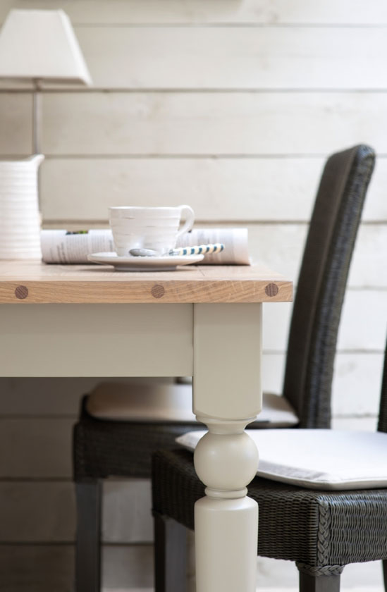 Nahaufnahme eines hellen Esstisches aus Holz mit weißer Tasse, Untertasse und Stuhl im gemütlichen Landhausstil