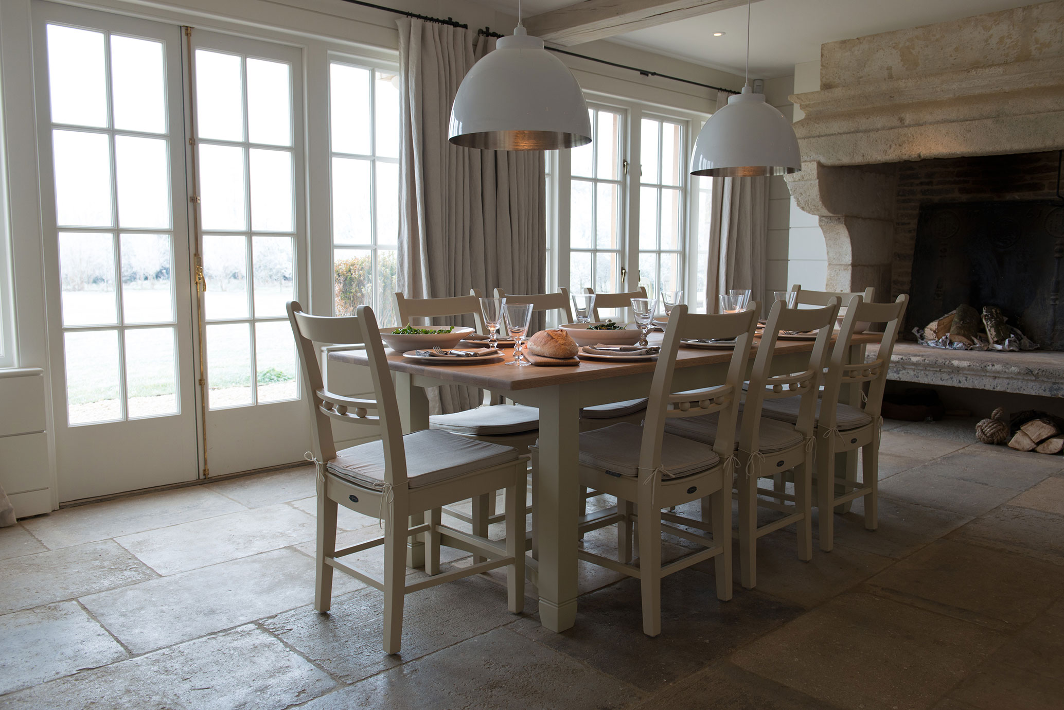 Heller Essbereich im Landhausstil mit großem Holztisch, acht Stühlen, gedecktem Tisch und Kamin