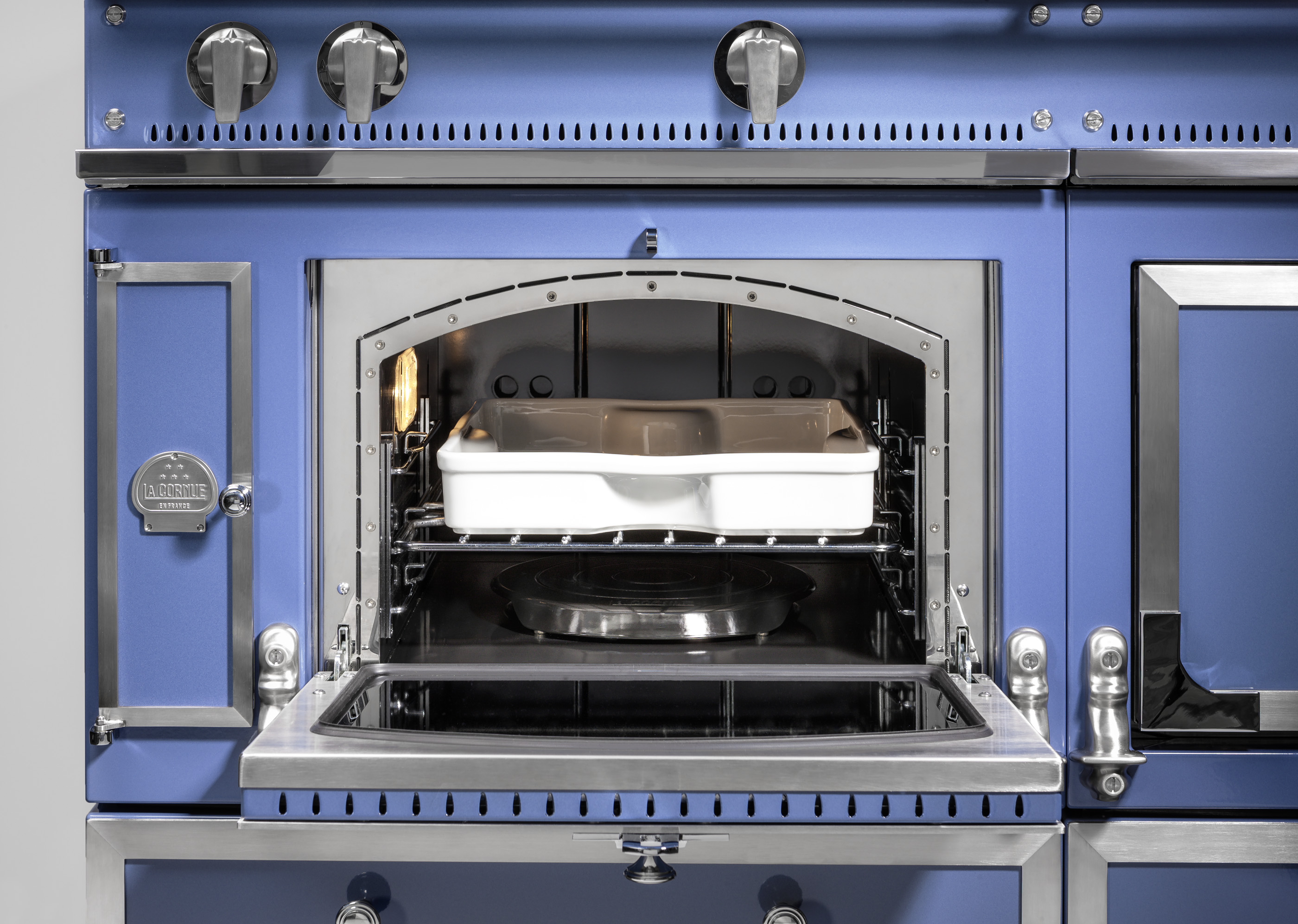 Detailaufnahme eines blauen Backofens mit geöffneter Tür und einer weißen Auflaufform auf dem Rost