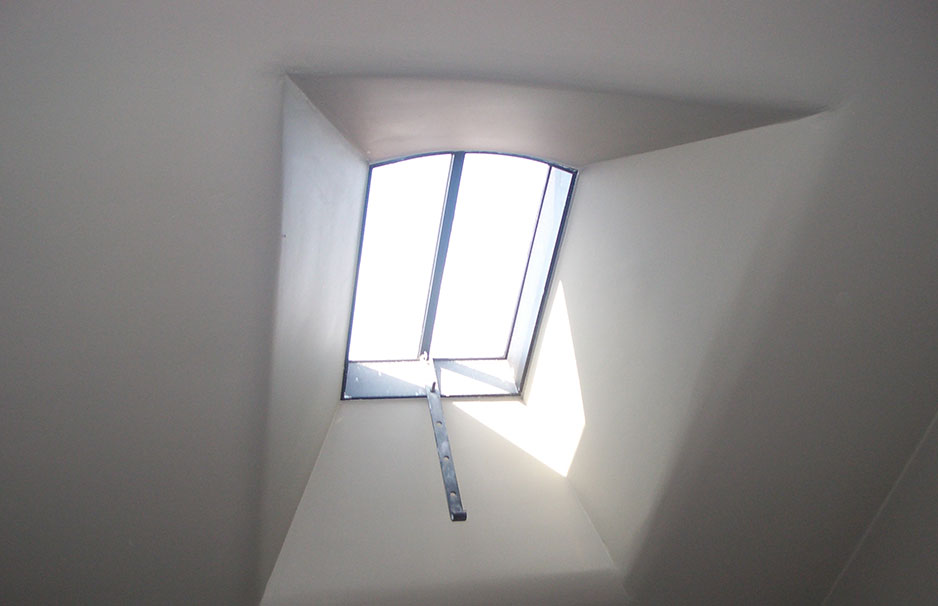 Geöffnetes Dachfenster mit Metallstange, durch das Sonnenlicht in einen Raum fällt