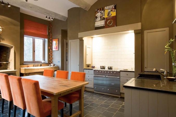 Geräumige Küche im Landhausstil mit großem Holztisch, orangefarbenen Stühlen, Natursteinboden und modernen Geräten