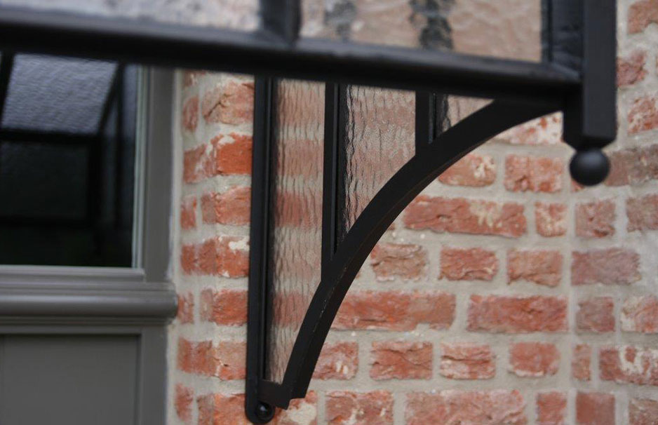 Vordach aus Metall und Glas an einer Backsteinwand, modernes Design mit gebogenem Metallträger, neben grauem Fensterrahmen