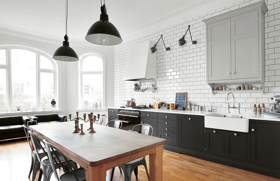 Helle, moderne Küche im Landhausstil mit weißen Fliesen, dunklen Unterschränken, großem Holzesstisch, Metallstühlen und zwei schwarzen Hängelampen