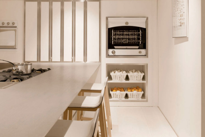 Helle, minimalistische Küche mit Gasherd, Backofen, weißen Stühlen und mehreren Körben mit Eiern und Orangen in einem Regal