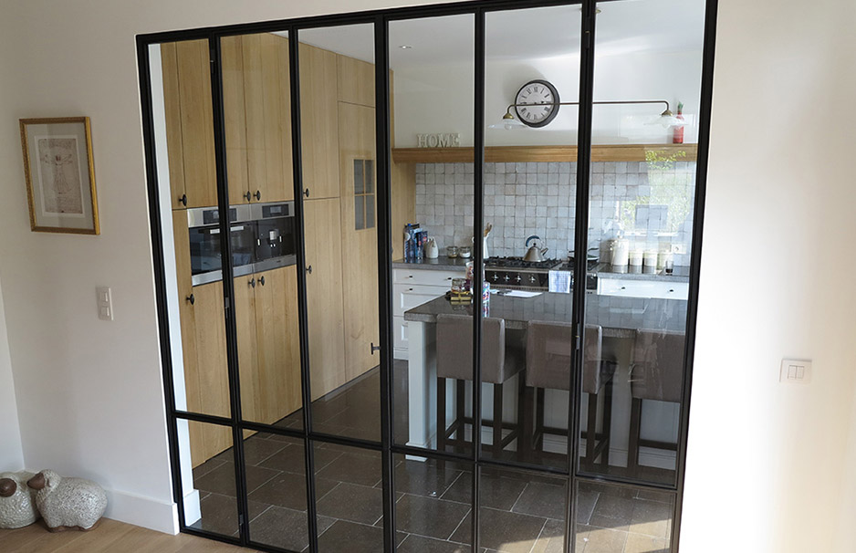 Schwarze Glas-Schiebetür trennt eine moderne Küche mit Holzschränken, weißer Arbeitsplatte und Barhockern vom Wohnbereich ab