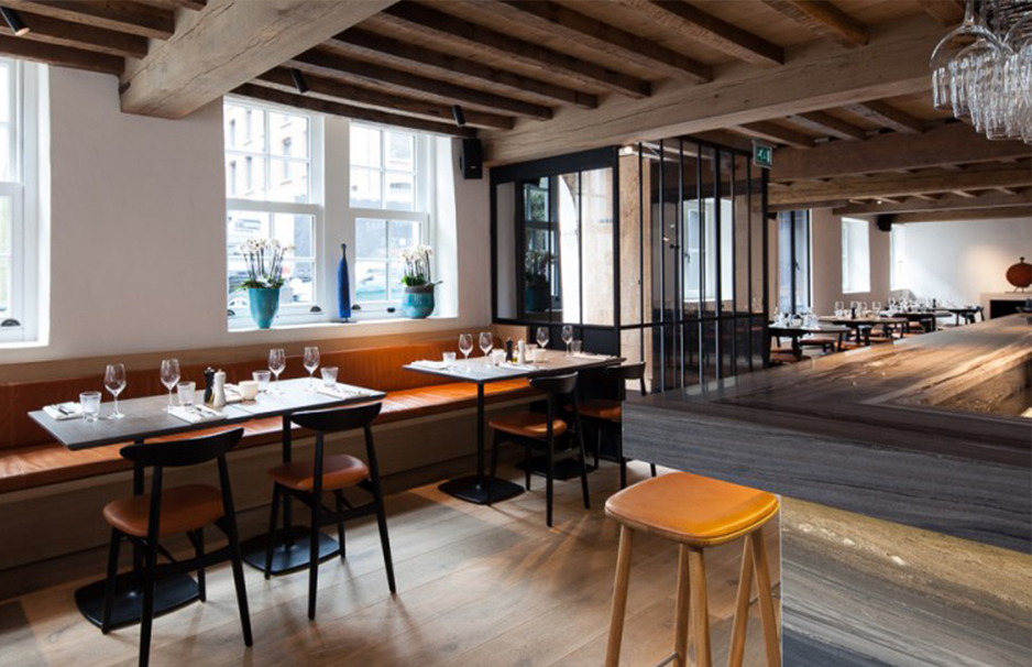 Innenaufnahme eines modernen Restaurants mit Holzbalkendecke, großen Fenstern, gedeckten Tischen und stilvoller Bar mit Hockern