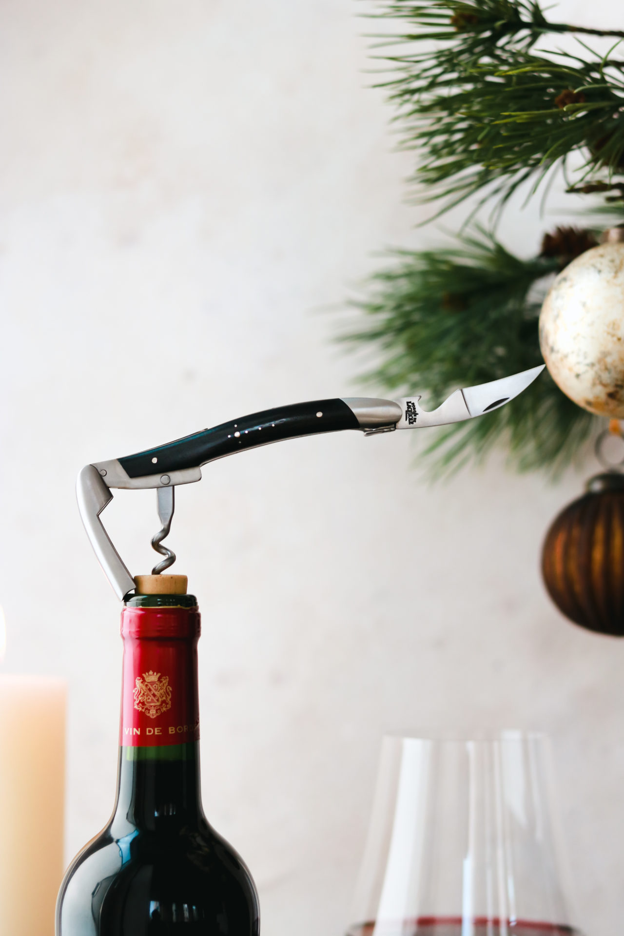 Kellnermesser öffnet eine Weinflasche, im Hintergrund Weihnachtskugel und Tannenzweige