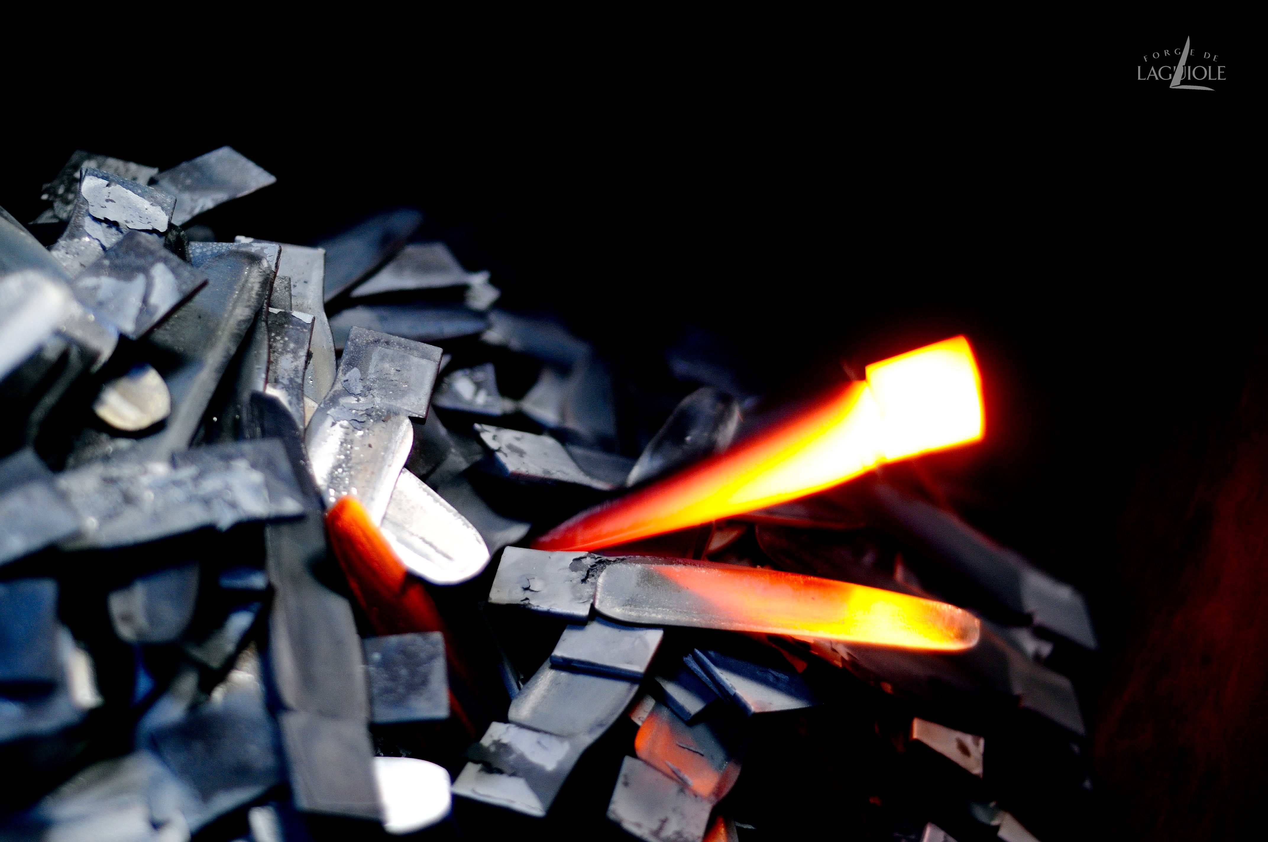 Glühender Stahlrohling liegt auf Metallstücken in einer Schmiede während der Klingenherstellung