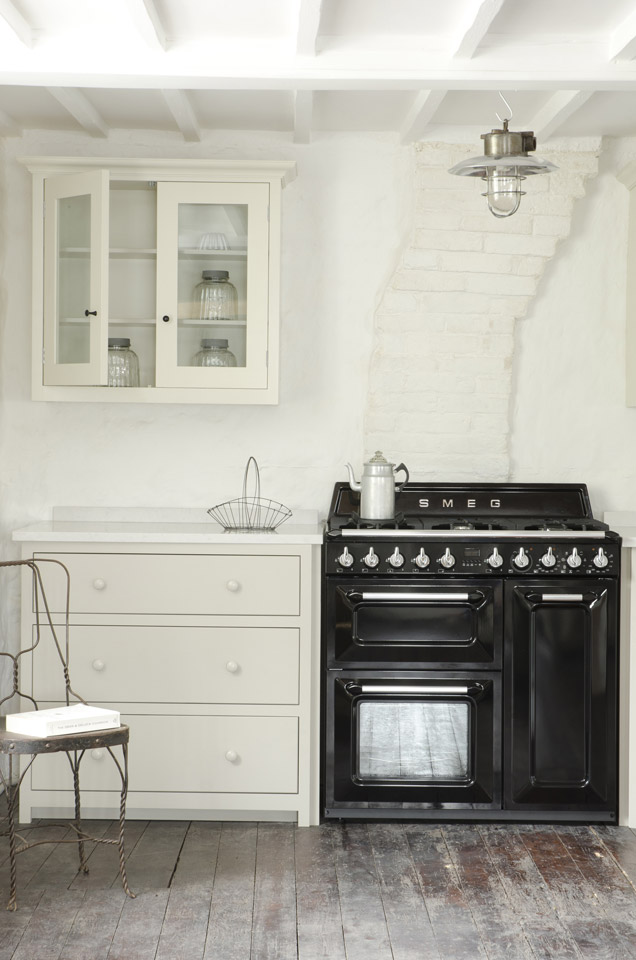 Helle Küche im Landhausstil mit cremefarbenem Unterschrank, Hängeschrank, schwarzem SMEG-Gasherd und rustikalem Holzboden