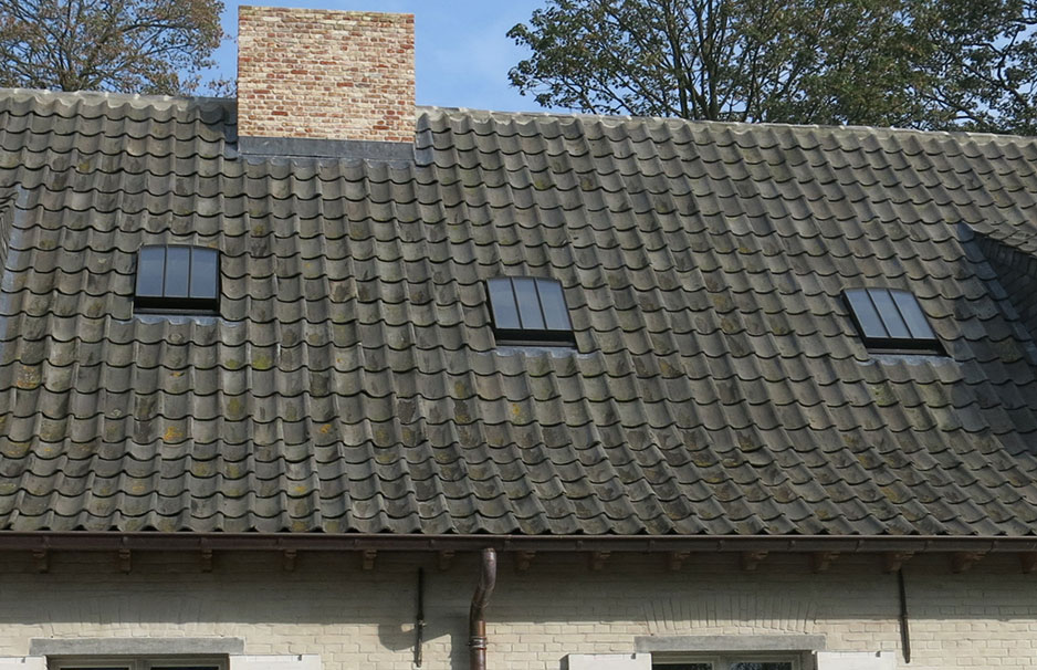 Schräges Ziegeldach mit drei kleinen rechteckigen Dachfenstern und einem gemauerten Schornstein