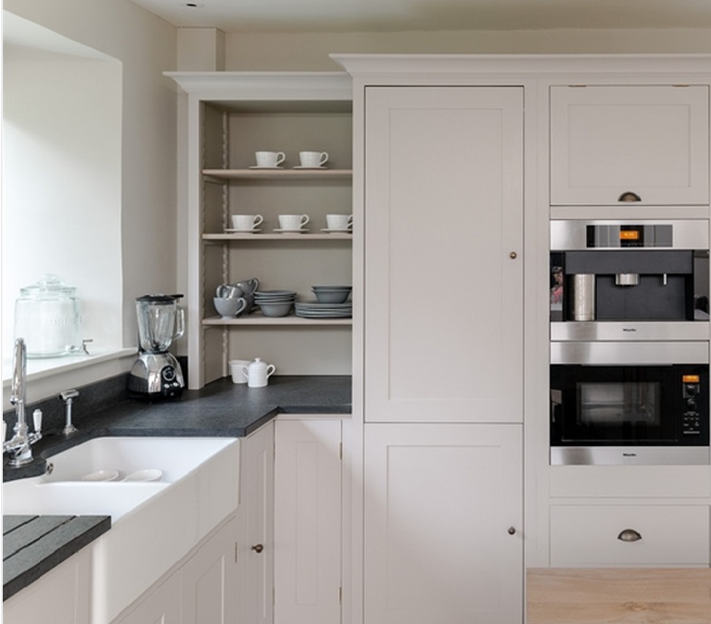 Helle Küche mit weißen Einbauschränken, offenen Regalen mit Geschirr, Spüle, Mixer und modernen Edelstahlgeräten wie Backofen und Kaffeemaschine