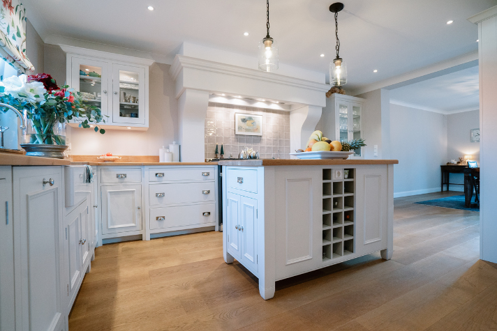 Offene, elegante Küche im Landhausstil mit weißer Einrichtung, Kochinsel und Holzfußboden