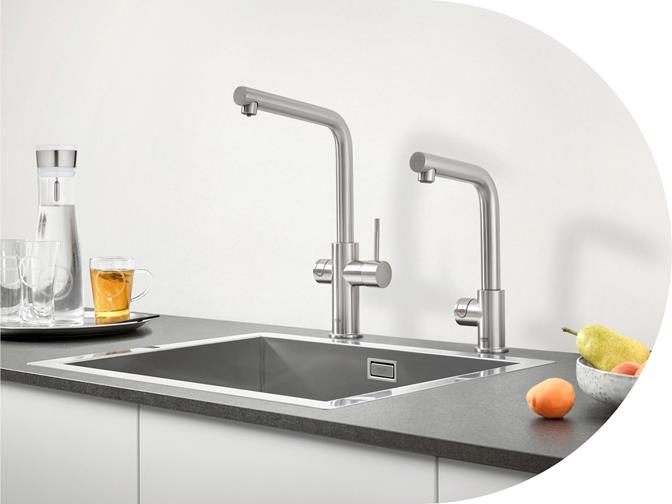 Küchenspüle mit zwei eleganten Edelstahl-Armaturen, daneben Obstschale und Gläser auf der Arbeitsplatte