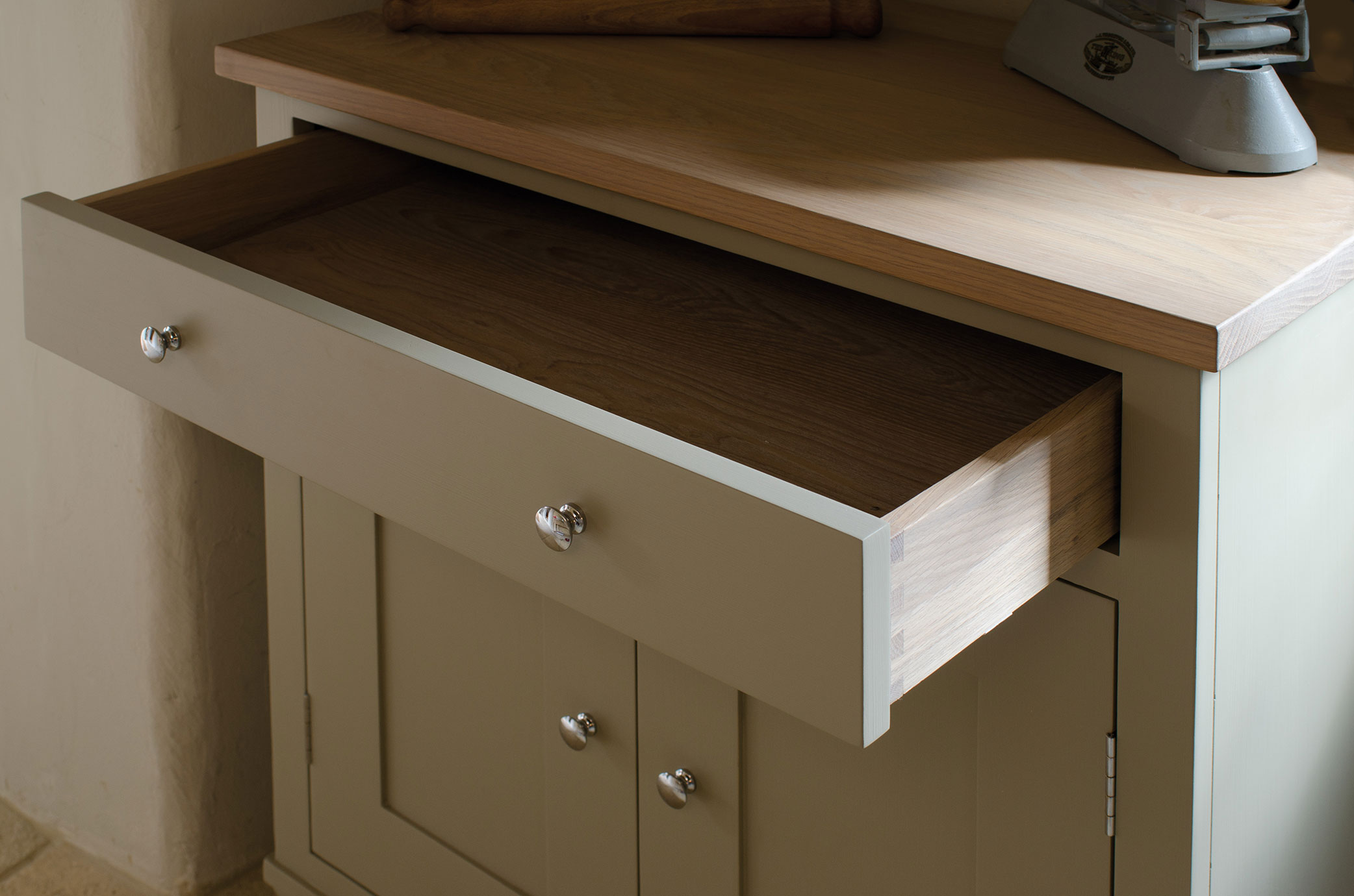 Beigefarbener Küchenunterschrank aus Holz mit geöffneter Schublade, silbernen Knäufen und heller Arbeitsplatte