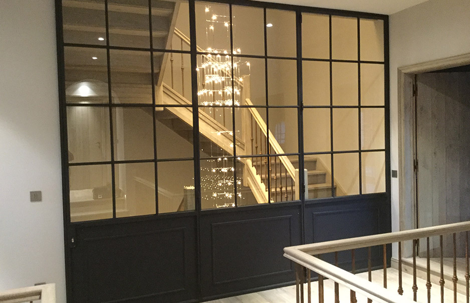 Moderne schwarze Stahl-Glas-Trennwand in einem Flur, dahinter eine Holztreppe mit dekorativer Beleuchtung