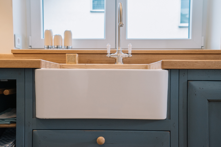 Weiße Keramikspüle mit traditionellem Wasserhahn in einer Küche mit Holzarbeitsplatte und blauen Unterschränken