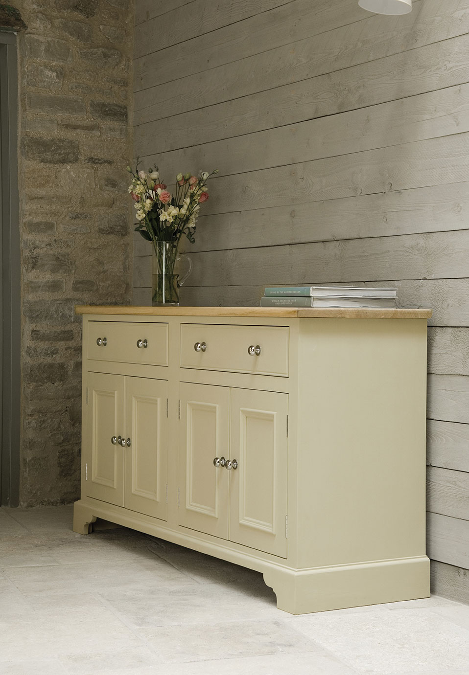 Sideboard im Landhausstil aus cremefarben lackiertem Holz mit vier Türen, vier Schubladen, Holzplatte, Blumenvase und Büchern