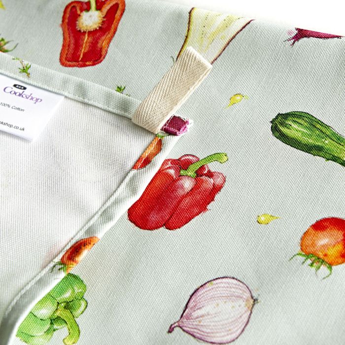 Detailaufnahme einer Küchenschürze mit buntem Gemüse-Muster aus Baumwolle, sichtbar sind Paprika, Zwiebel und anderes Gemüse