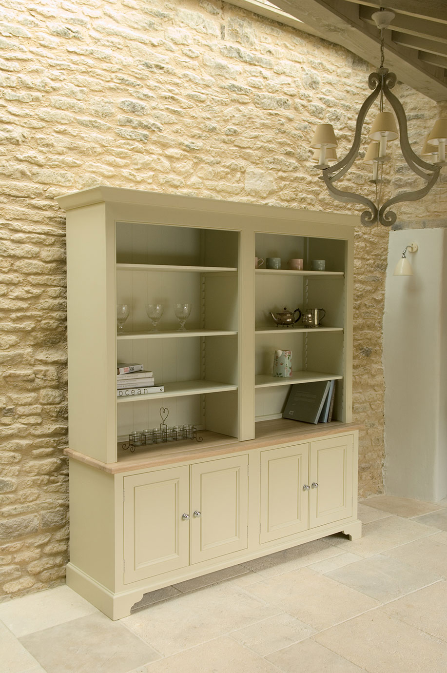 Buffet im Landhausstil aus Holz mit cremefarbenem Anstrich, offenen Regalen, Unterschränken, dekoriert mit Gläsern, Tassen, Teekanne, Büchern und Accessoires, vor einer Steinwand