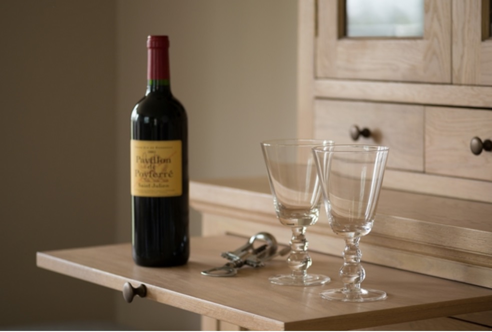 Eine Flasche Rotwein, zwei leere Weingläser und ein Korkenzieher stehen auf einer ausgezogenen Holzschublade vor einem Holzschrank.