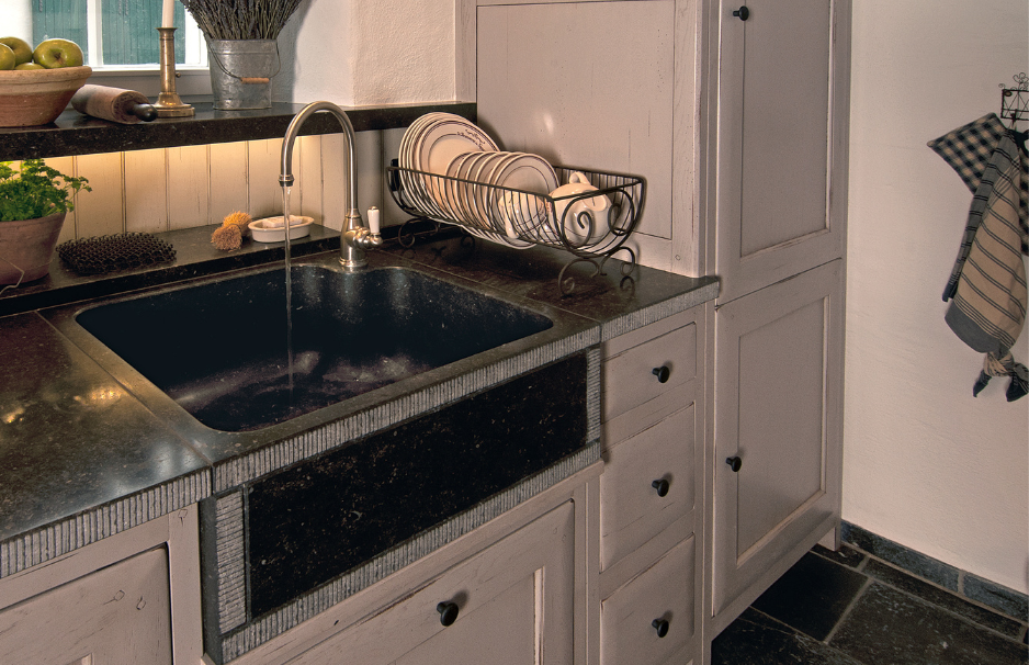Küchenspüle aus schwarzem Naturstein mit Wasserhahn, Vintage-Unterschrank und Metall-Geschirrkorb neben Küchenutensilien