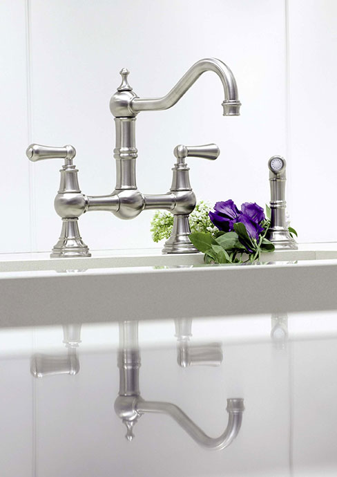 Küchenarmatur aus Edelstahl mit zwei Griffen und gebogenem Auslauf, daneben lila Blumen auf der Arbeitsfläche