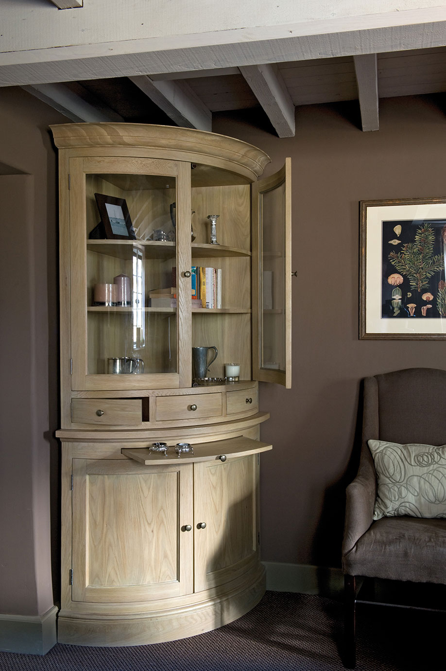 Eckvitrine aus Holz mit Glastüren und mehreren Schubladen, dekorativ bestückt, in einer modernen Wohnzimmerecke platziert