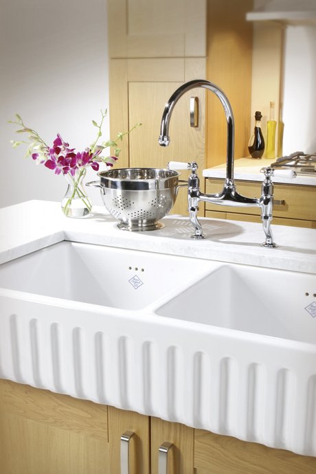 Doppelspülbecken aus Keramik mit glänzender Chromarmatur, Abtropfsieb und Vase mit lila Orchideen auf einer Arbeitsplatte in einer modernen Küche