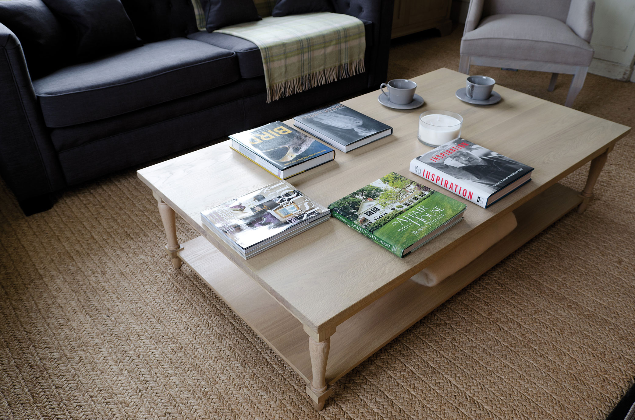 Heller Holzcouchtisch im Wohnzimmer, dekoriert mit mehreren Bildbänden, einer großen weißen Kerze und zwei grauen Kaffeetassen