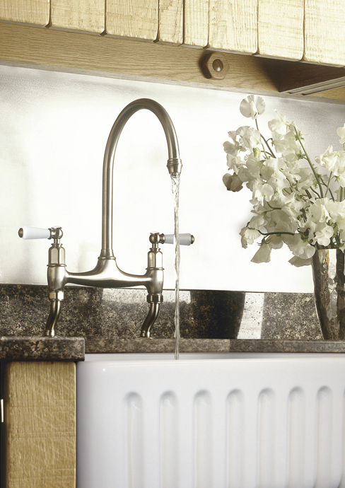 Nahaufnahme einer modernen Küchenarmatur mit Wasserstrahl über einer weißen Keramikspüle und einem Blumenarrangement auf der Arbeitsplatte