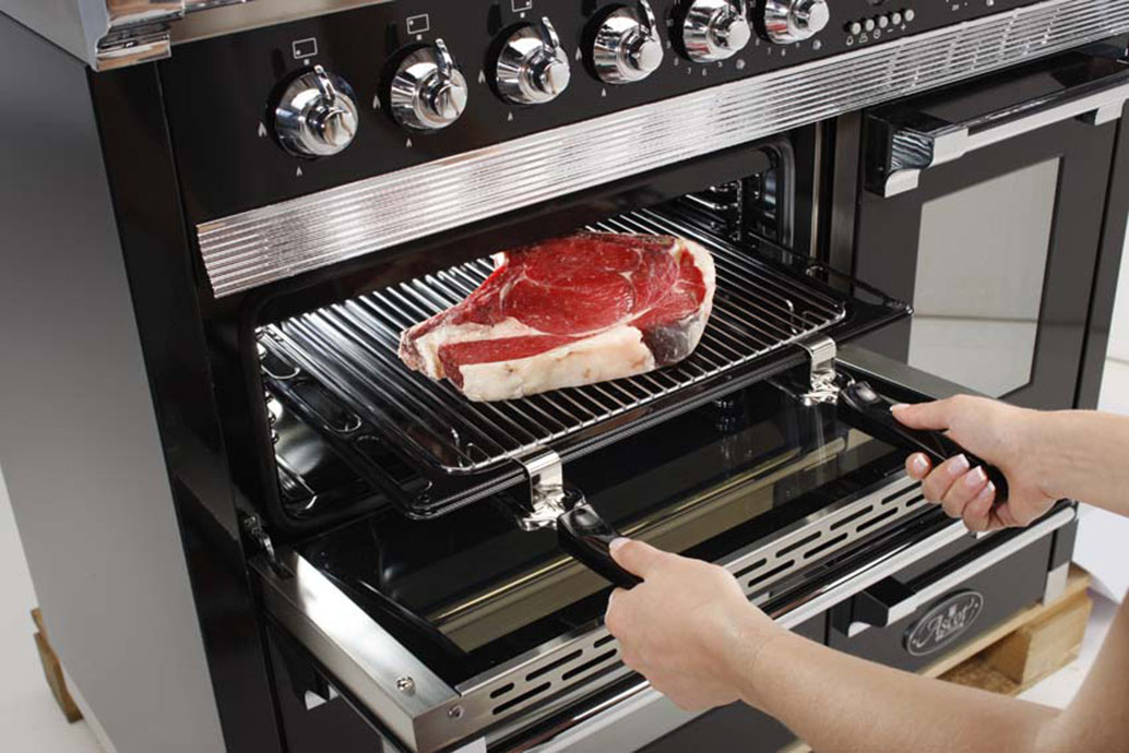Person schiebt ein großes, rohes Steak auf einem Grillrost in einen modernen Backofen