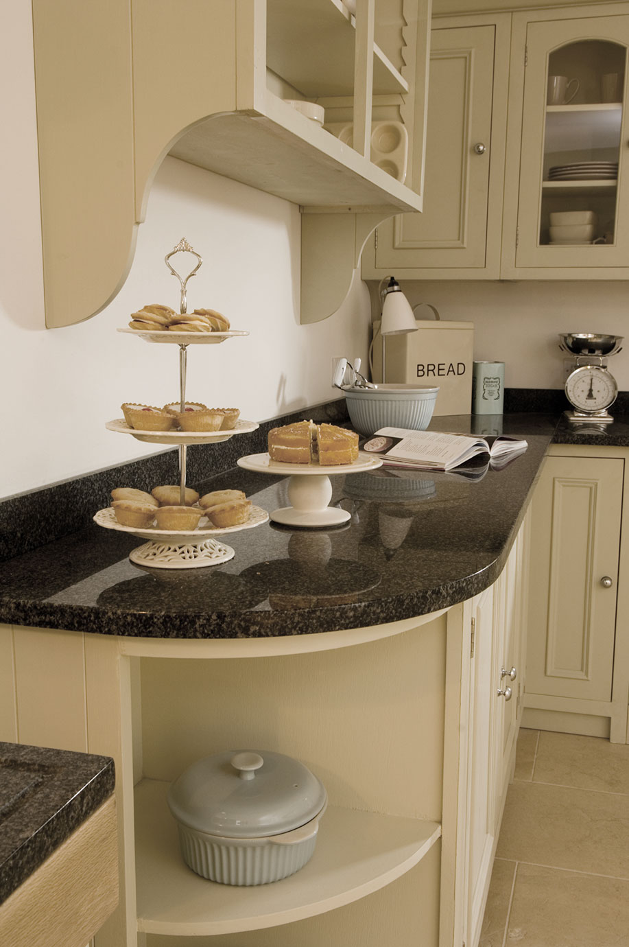 Helle Küche im Landhausstil mit Granitarbeitsplatte, Etagere mit Gebäck und Kuchen, Küchenwaage, Brotkasten und Kochbuch